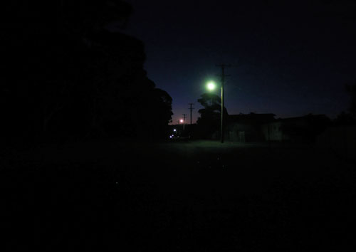 A street light glows against a small beach town road.