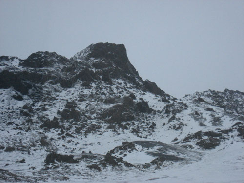 A proud and ominous black rock cliff in Iceland, covered in snow.
