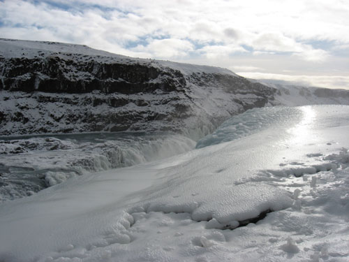A shiny cliff of ice hangs over wintery Gullfoss Falls in Iceland.