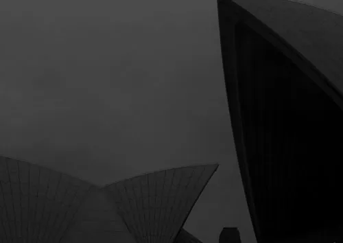 A low contrast night photo of the Sydney Opera House in black and white with a large fraction of a shell dominating the front of the photo and a smaller silhouette of a double shell in the background.