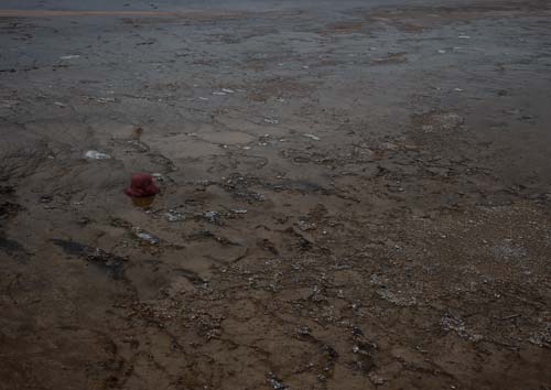 A child's pink hat sits lonely and isolated in a geyser's mud flats, too far for anyone to reach.