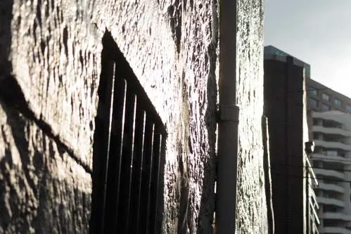 Bright sunlight reflects on a raw sandstone building with the rest in deep shadow.